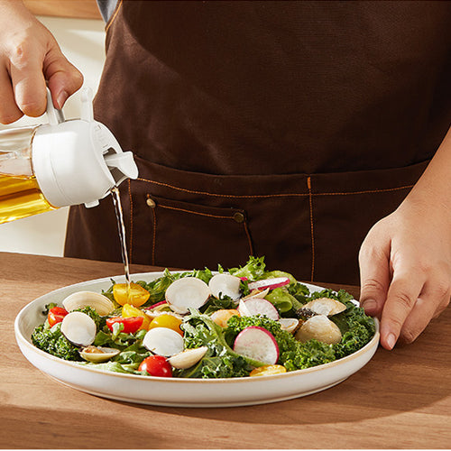 Person dressing a salad with a white dressing container on a wooden table.