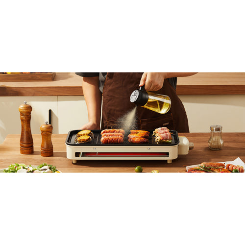 Person cooking on a portable grill with a bottle of oil in a kitchen setting